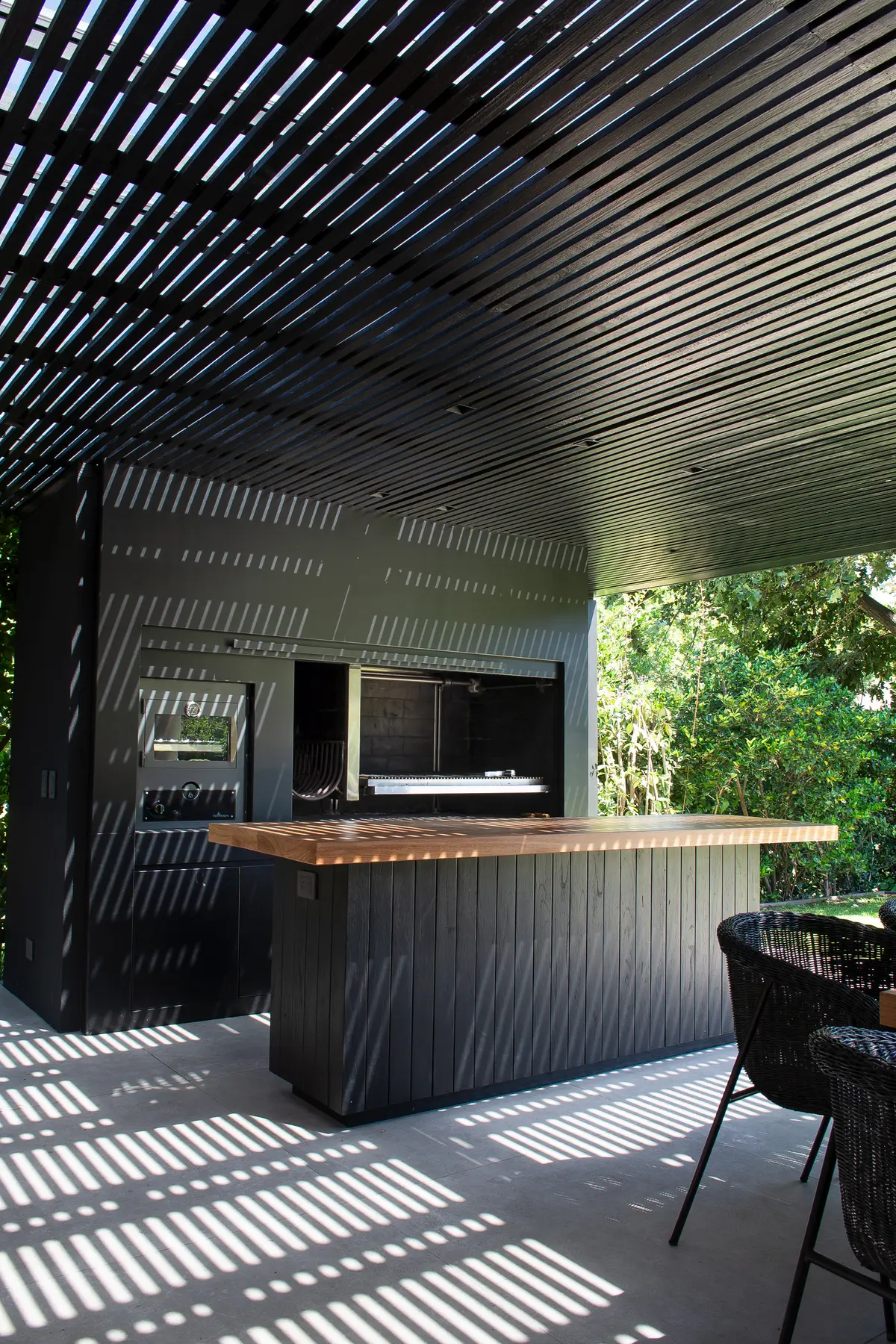 área de churrasco moderna com pergolado de madeira e sombras geométricas — projeto Quincho SA, por Estudio Junor, em Pilar